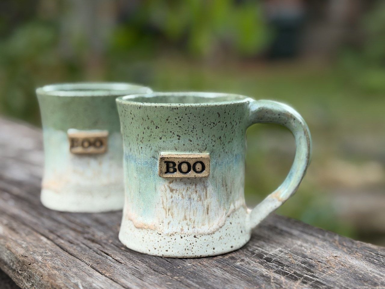 Two green and cream mugs labeled Boo on a wooden table.